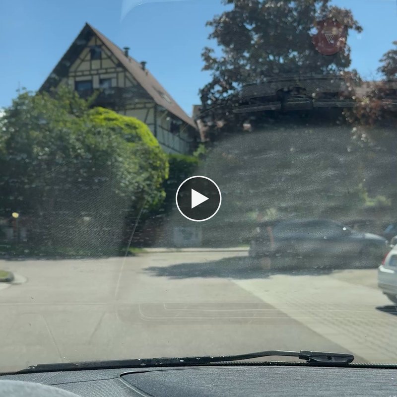 Vorschaubild des zweiten Eröffnungsvideos: Blick durch die Windschutzscheibe eines Autos auf eine sonnige Straße mit Fachwerkhaus